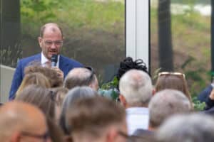 feldmann_robert_6372 | Quadriga Hochschule Berlin Mann mit Mikrofon spricht vor einer Menschenmenge, teilweise mit Blick auf ihn, im Freien.