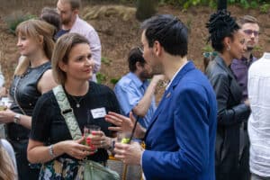 feldmann_robert_6447 | Quadriga Hochschule Berlin Zwei Personen unterhalten sich bei einer Veranstaltung im Freien, umgeben von weiteren Gästen und grüner Umgebung.