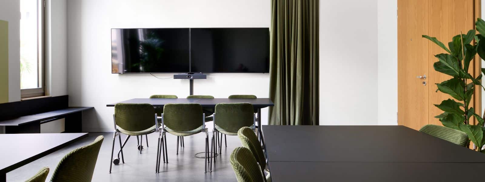 11 Moderne Besprechungsraum mit schwarzen Tischen, grünen Stühlen, einem großen Bildschirm und einer Pflanze in der Ecke.