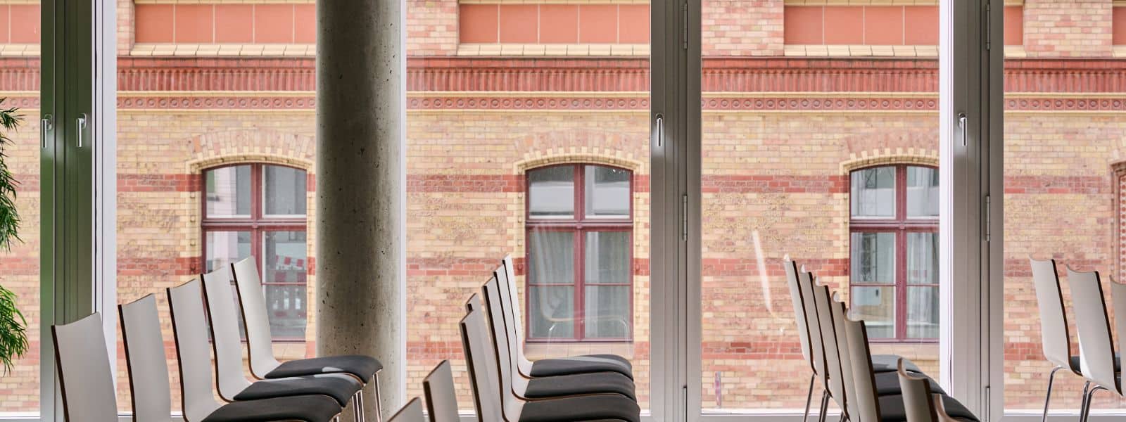 41 Leere Stühle stehen in einem modernen Raum mit großen Fenstern, die auf eine historische Backsteinfassade blicken.